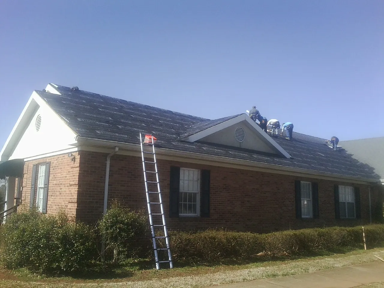 Crew tearing shingles off a brick ranch roof with a ladder set — Metal Roof Repair work by our crew in Saint Charles