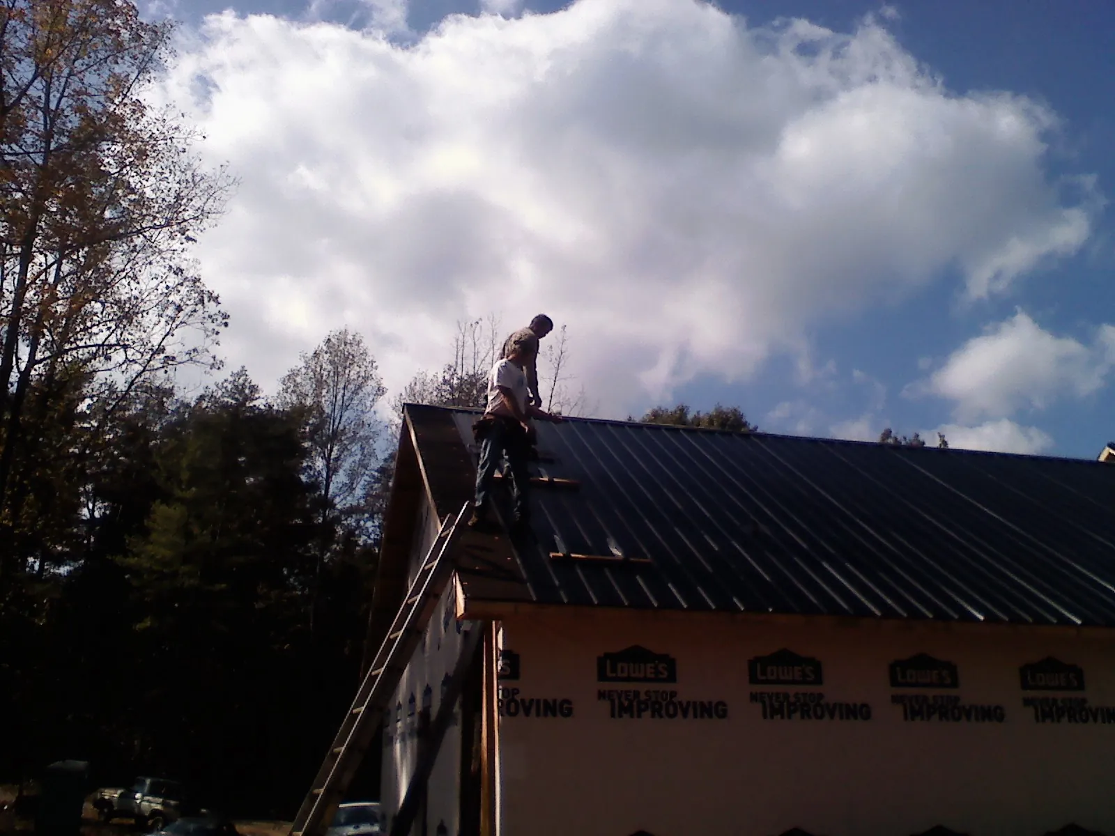 Roofer fastening dark metal panels high against a cloudy sky, from a Roof Inspection job in Saint Charles