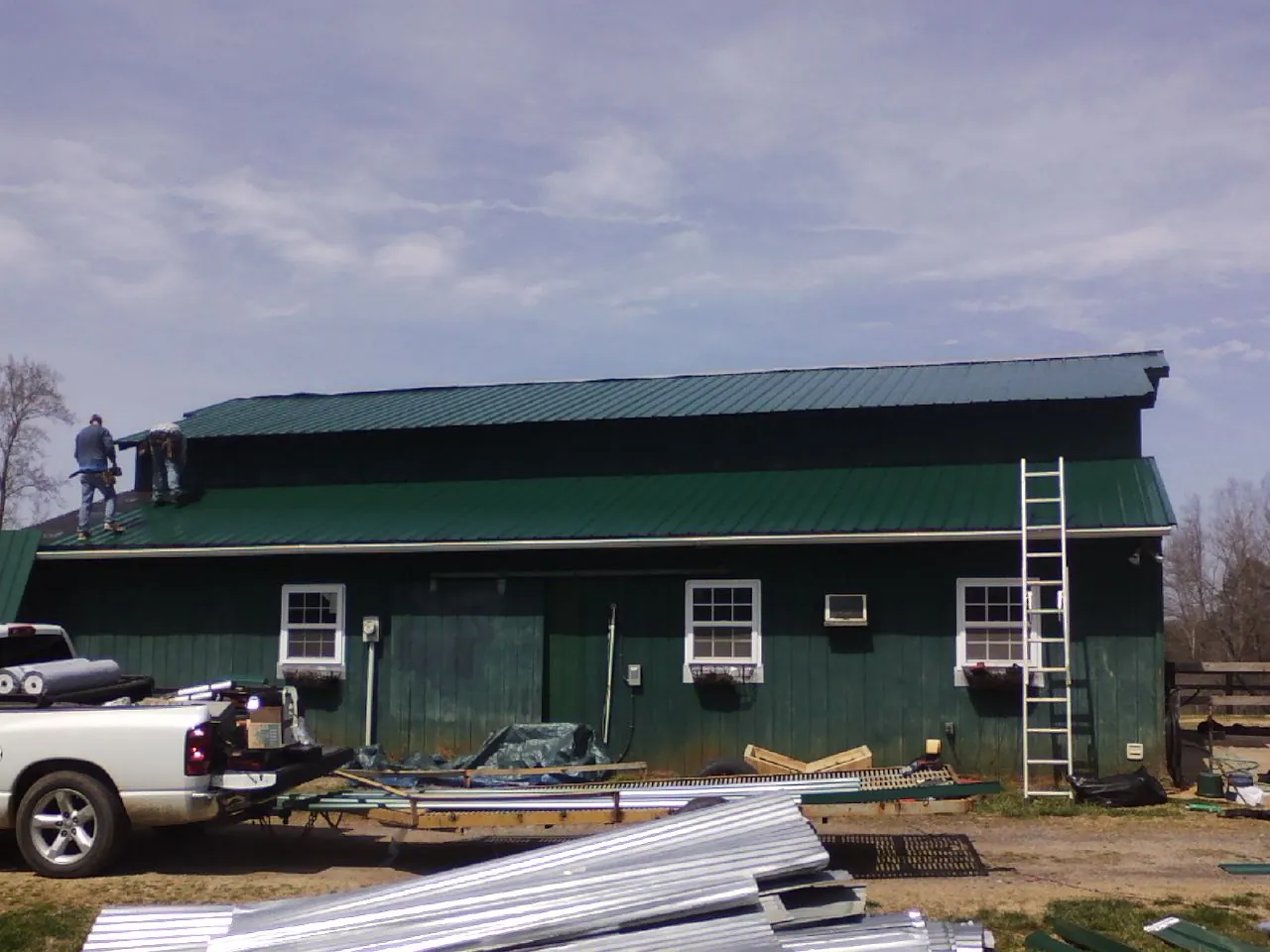 Crew installing green metal roofing on a large green barn in Saint Charles