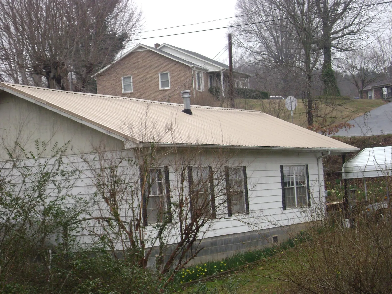 Tan metal roof on a white sided house set into a hillside — Commercial Roofing by Roofing Brothers in Saint Charles